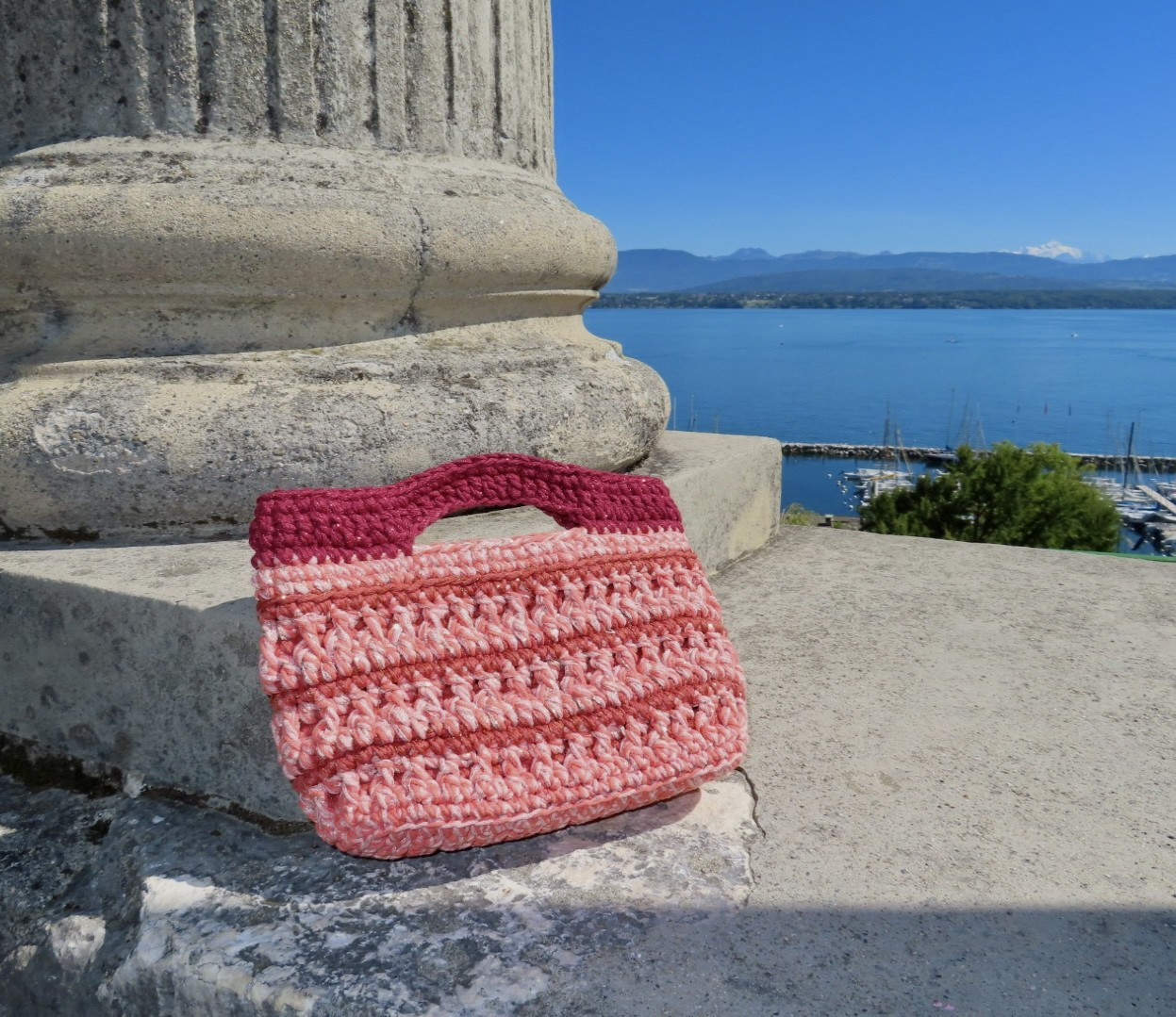 A handmade crochet bag in pink recycled cotton, photographed by the lake