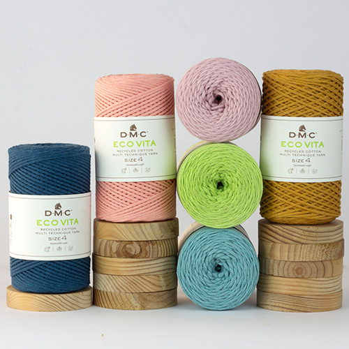 Several colourful spools of DMC Eco Vita 4 recycled cotton yarn arranged on pastel blocks